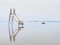 Old steel slide in lake. Chrome ladder tower with sliding track, big granite stones around. Royalty Free Stock Photo