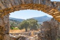 Old stone arch amonst remains of tumbled down structure, through which beyond olive trees is Mount Zeus Royalty Free Stock Photo