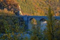 Old stone bridge over the mountain river across autumn forest, hills, and sunset sky. Natural background. Travel, movement, archit Royalty Free Stock Photo