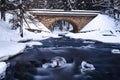 Bridge over river in winter, surrounded by forest and snow Royalty Free Stock Photo