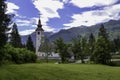 Old stone church on the shore of a mountain lake. Green mountain range and blue sky with white clouds Royalty Free Stock Photo