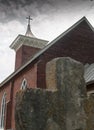 Old stone cross and brick church building on cloudy day Royalty Free Stock Photo