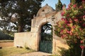 Old stone entrance gate in cemetery, White fence with green metal doors at sunset light. European Catholic Cemetery