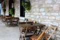 Old stone exterior wall of building with rows of mismatched chairs and tables set against it