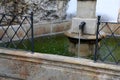 Old stone fountain for watering horses and horses with a spout of metal pipes. black metal fencing