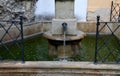 Old stone fountain for watering horses and horses with a spout of metal pipes. black metal fencing