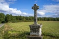 Old stone grey cross standing against background scene of green forest and field