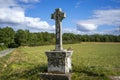 Old stone grey cross standing against background scene of green forest and field