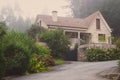 Old stone house with beautiful garden in morning fog. Rural cottage in village in forest. Cozy residence with trees and flowers. Royalty Free Stock Photo