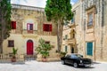 Old stone house with colorful windows and black classic style convertible car - Mdina, Malta