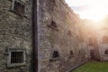 Old stone jail wall with small windows with metal bars. Sun flare. Law correction facility with hard living conditions. Cork Gaol