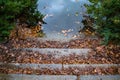 Old stone stair covered with wet fall leaves near calm pond water surface with blurred reflection. Stairway to lake. Royalty Free Stock Photo