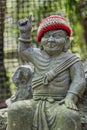 Old stone statue of Buddhist monk wearing knitted hat pointing the finger up.