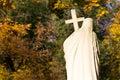 Old stone statue with cross, autumn leaves background.