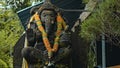 Old stone statue of Ganesha covered with moss with a wreath of yellow flowers on his neck standing on the street Royalty Free Stock Photo