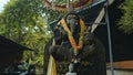 old stone statue of Ganesha covered with moss with a wreath of yellow flowers on his neck standing on the street Royalty Free Stock Photo