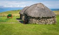 An old stone thatched cottage with the sea and a horse carriage in the background