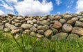 Old Stone Wall With Green Grass In Front And Blue Sky With Clouds Above