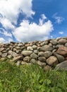 Old Stone Wall With Green Grass In Front And Blue Sky With Clouds Above, Vertical Image