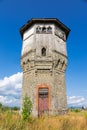 Old stone water tower with windows and a wooden roof against the background of blue sky and green trees on a sunny summer day Royalty Free Stock Photo