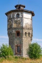 Old stone water tower with windows and a wooden roof against the background of blue sky and green trees on a sunny summer day Royalty Free Stock Photo