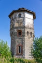 Old stone water tower with windows and a wooden roof against the background of blue sky and green trees on a sunny summer day. Royalty Free Stock Photo