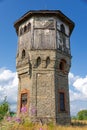 Old stone water tower with windows and a wooden roof against the background of blue sky and green trees on a sunny summer day Royalty Free Stock Photo