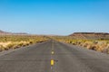 Old straight asphalt road with yellow dashed line leading into the horizon