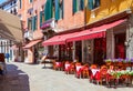 Old street with colorful facades and red tables of cafe at a sunny morning, Venice, Italy