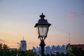 An old style lamp post in focus with the rest of town not in focus in the background as the sun sets over the city of Stettin,