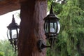 Old style metallic lanterns attached to brown wooden pillar, with green trees in the background Royalty Free Stock Photo