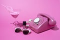 Old style rotary telephone on pink background with cocktail, sunglasses and nail polish Royalty Free Stock Photo