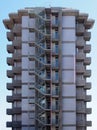 an old tall concrete apartment block with repeating concrete balconies and external fire escape stairs with metal railings against Royalty Free Stock Photo