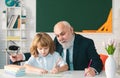 Old teacher and young schoolboy doing homework assignment at school. Teachers day. Royalty Free Stock Photo
