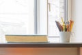 Old thick book and plastic gray cup with pencils on desk at window. Copy space for text Royalty Free Stock Photo