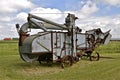 An old threshing machine resides in a field with a freight train passing in the background Royalty Free Stock Photo