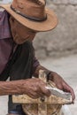 Old Tibetan man cleaning ancient wooden prayer wheel