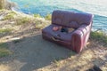 Old torn sofa with burgundy color. Red ruined couch on sea shore. Hole in seat and torn foam. Abstract composition of old couch