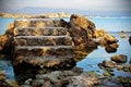 Old tower stone stairs in blue sea water background with rocks and mountain on the horizon