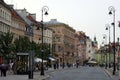 Old town square buildings lit by the sun in a row, people in the market square