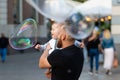 Bearded man with a child on his hands watches and rejoices at the gigantic soap bubbles, Old Town Square, Riga, Latvia