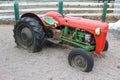 An old tractor colored green and red with flat rear tires on a farm parked in gravel next to a fence