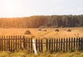 An old tractor plows a field in a village, haystacks and an old fence stand on the field, there is a forest on the horizon Royalty Free Stock Photo