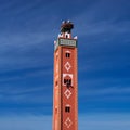 Old traditional terracotta minaret with storks nest on the top and arabic man painting ornament from the window. Morocco