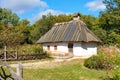 Reconstruction of an old traditional Ukrainian rural house with a thatched roof against the backdrop of a summer garden with a Royalty Free Stock Photo