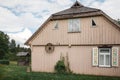 Old traditional wooden house with windows and shutters, rear view. An old carriage wheel is hung on the wall, the roof is covered