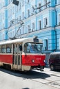 An old tram rides along a street with a blue house