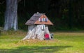 old tree stump turned into a garden fairy gnome house in the middle of Grass field with tiny bigfoot