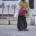 Old Tunisian woman in worn clothes carries a plastic sack over her shoulder