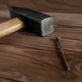 Old used hammer, wooden handle, metal head and rusty nail on wooden backdrop